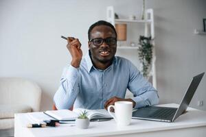 Sitting,, and ,smiling. With pen in hand. Businessman is working in the office by laptop photo