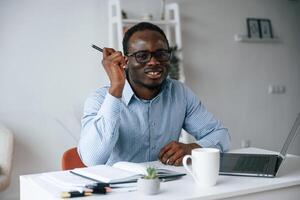 Sitting and smiling. With ,pen ,in hand. Businessman is working in the office by laptop photo