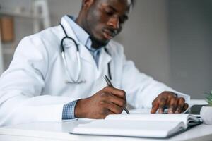 Filling in the document, writing, by, using pen. Black man as doctor in the clinic office photo