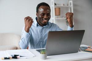 Celebrating, success... With hands up. Businessman is working in the office by laptop photo