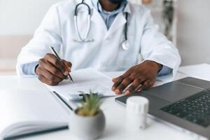 Writing information into the document. Black man as doctor in the clinic office photo