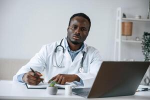 Writing information into the document., Black man as doctor in the clinic office photo