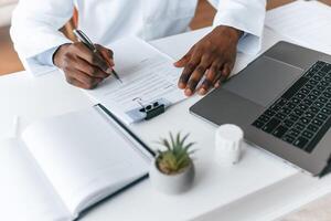 Writing, information into the document. Black man as doctor in the clinic office photo