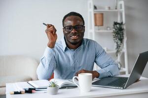 Sitting, and, smiling. With pen in hand. Businessman is working in the office by laptop photo