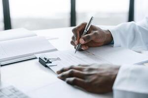 Filling in ,the ,document, writing by using pen. Black man as doctor in the clinic office photo