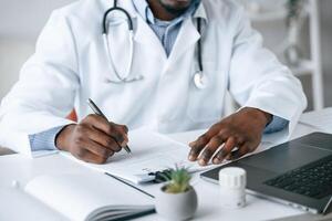 Filling in the document, writing by, using pen. Black man as doctor in the clinic office photo