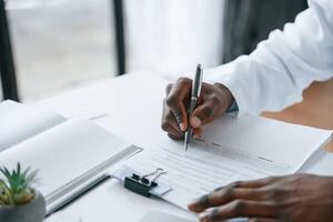 Filling, in the document, writing by using pen. Black man as doctor in the clinic office photo