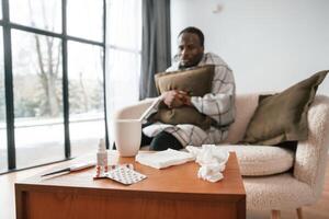 Sitting ,on sofa, holding, pillow. Sick black man is at home photo