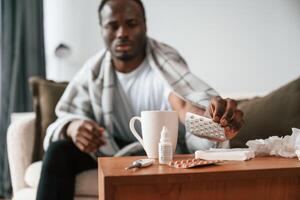 Holding pills ,that are on, the table. Sick black man is at home photo