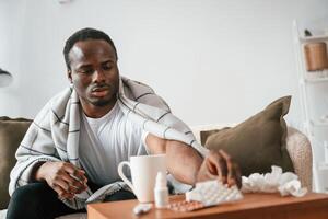 Holding ,pills that are on the ,table. Sick black man is at home photo