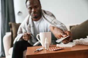 Holding, pills ,that are on the table. Sick black man is at home photo