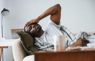 Lying down, on the sofa. Sick black man is at home photo
