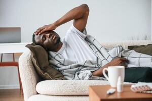 Lying, down on t,he sofa. Sick black man is at home photo