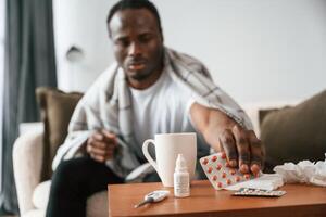 Holding pills, that, are on the table. Sick black man is at home photo