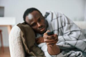 Holding ,,TV remote controller. Lying down. Sick black man is at home photo