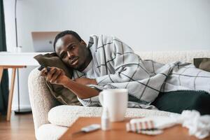 Holding, TV remote controller. Lying down. Sick black man is at home photo