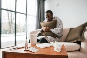 Sitting, on sofa, holding pillow. Sick black man is at home photo
