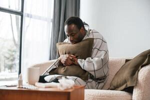 Sitting on, sofa, holding pillow. Sick black man is at home photo