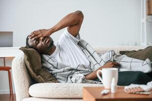 Lying, down on the sofa. Sick black man is at home photo