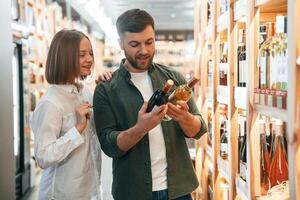 Choosing between two ,different bottles. Man and woman in the wine shop photo