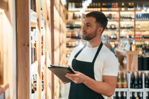 Quality control, with, notepad. Wine shop owner in white shirt and black apron photo