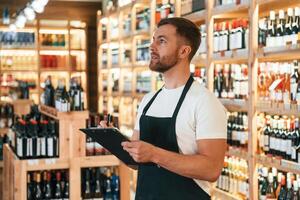 Quality, control, with notepad. Wine shop owner in white shirt and black apron photo