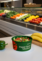 A fresh salad in a green paper bowl sits on a counter in front of a produce display psd