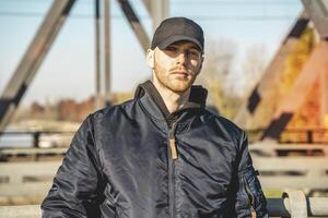 portrait of a young rapper with cap looking at camera on a bridge photo