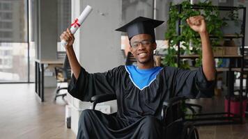 Joyful African American student in wheelchair celebrating graduation, smiling and raising arms with diploma in hand after academic achievement video