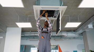 Skilled African American technician in uniform and helmet installs a ceiling air conditioning unit video