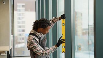 African American worker installing window with level video