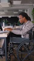 African American freelancer programmer in a wheelchair coding on a laptop at a desk in a modern coworking space video