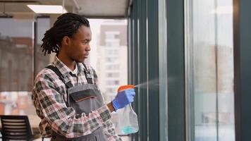 Janitor in work uniform and gloves uses a squeegee to clean a tall window in office video