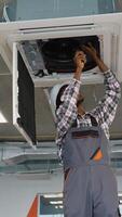Skilled African American technician in uniform and helmet installs a ceiling air conditioning unit video