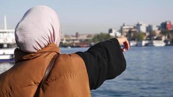 Woman in hijab points towards city skyline over calm water video