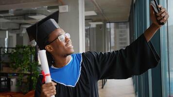 African American student in graduation cap and gown proudly takes selfie while holding diploma video