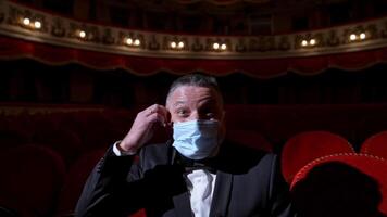 Happy actor puts off medical mask and throws it. Man in costume sitting in the empty theatrical hall and invites joyfully to come to performance. The end of pandemic. video