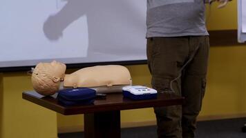 Medic talks in training center. Mannequin and medical equipment on a little table. Instructor explaining the reanimation procedure near the doll model. video