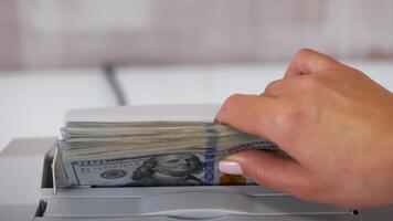 Electronic equipment for counting paper money. Bank worker putting a bundle of one hundred dollar bills into the counting machine for calculation. video