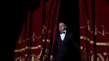 Portrait of a host. Man actor in black costume appears on stage and begins the speech in bright light spot in the theater. video