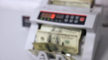 Counting dollar bills. Money counting machine with 100 dollar banknotes. Female's hand holds a pack of US national paper currency. Finance concept. Close-up. Blurred background. video