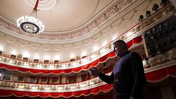 Man is giving interview in the opera house. Middle-aged actor talking to someone while standing on stage on classical theatre background. video