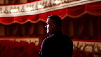 Actor rehearsing in front of empty auditorium. Back view of a man on stage against spotlight in the theater. Male performer speaking on scene. Close-up. video