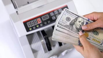 Bundle of one hundred dollar banknotes. Female's hands holding a large sum of money of dollar bills on the background of automatic counting machine. video
