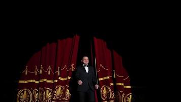 Theatrical stage. Man in costume appearing on a scene and presents the performance in light spot on dark background. video