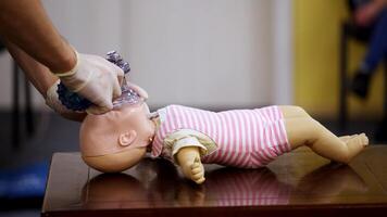 Demonstration of cpr on a baby model. Instructor in medical gloves showing the right breathing exercise on a dummy in training center. Side view. video