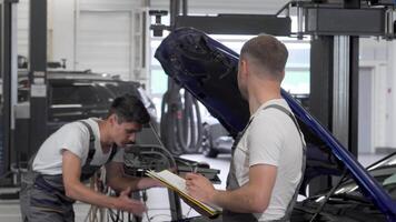 Two mechanics collaborate on repairing a broken automobile in a bustling garage video