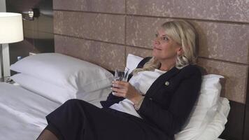 An elegant woman relaxes on a plush hotel couch while sipping water video