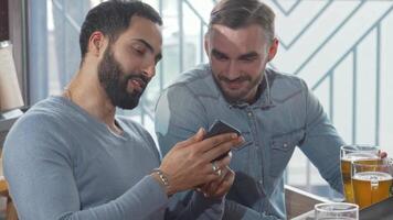 Two male friends enjoying beers while sharing a smartphone video