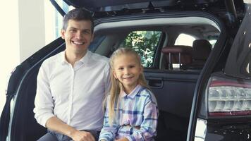 Charming father and daughter joyfully sitting on the open trunk of a sleek car video